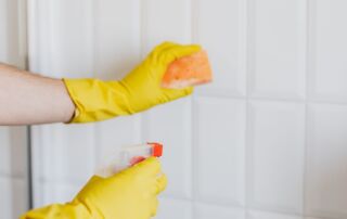 Gloved hands scrubbing white bathroom tiles to remove hard water stains in a Treasure Valley home