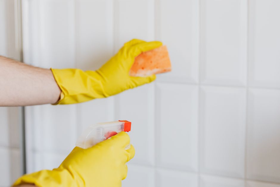 Gloved hands scrubbing white bathroom tiles to remove hard water stains in a Treasure Valley home